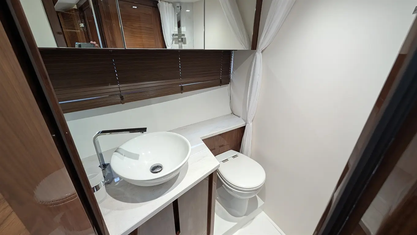 Modern bathroom featuring a white circular basin, toilet, and a sleek wooden countertop with a mirror and window blinds.